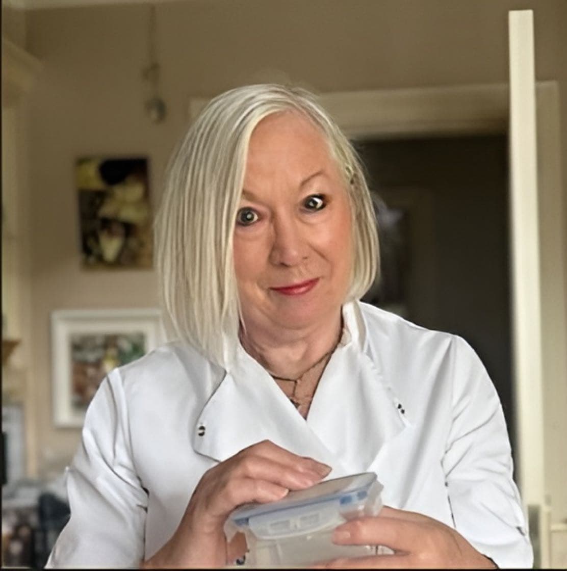Dóirín in chef whites in her home kitchen, holding a prepared dish in a sealed container.
